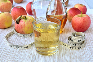 Apple cider vinegar diluted with water, slimming drink in a glass, ripe apples, measuring tape in inches, on a table.