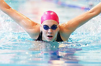 donna che nuota a delfino con cuffia rosa in piscina